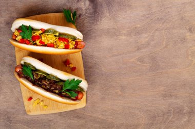 Farklı malzemeli lezzetli sosisler: turşu, kızarmış soğan, domates ve havuç, ahşap arka planda fotokopi alanı ile yeşil. Düz yat. Fast food konsepti üst görünüm.