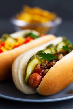 Turşulu Danimarka sosisi, kızarmış soğan, sos ve ketçap bir restoranın ahşap tepsisinde. Gri tabakta sosisli sandviç. Fotokopi uzayı ile fast food konsepti. dikey