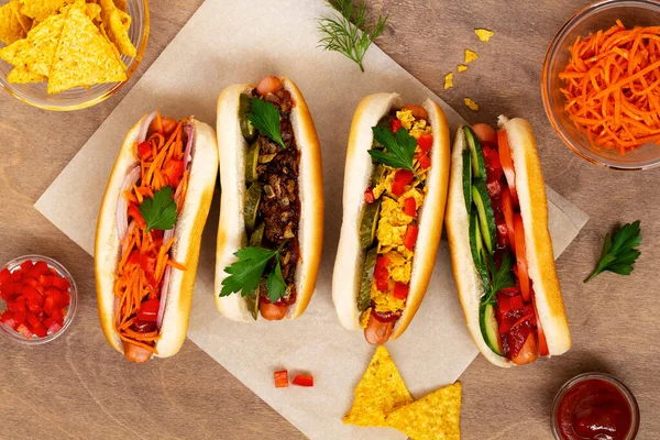 Farklı malzemeli ev yapımı lezzetli sosisler: turşu, kızarmış soğan, domates ve havuç, ahşap arka planda fotokopi alanı olan yeşil havuç. Düz yat. Fast food konsepti üst görünüm.