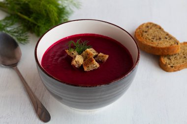 Sebzeli, sebze çorbası ve kızarmış ekmek. Beyaz zemin üzerinde ekmek ve kaşık olan gri pancar kremalı çorba kasesi. Fotokopi alanı ile sağlıklı diyet öğle yemeği.