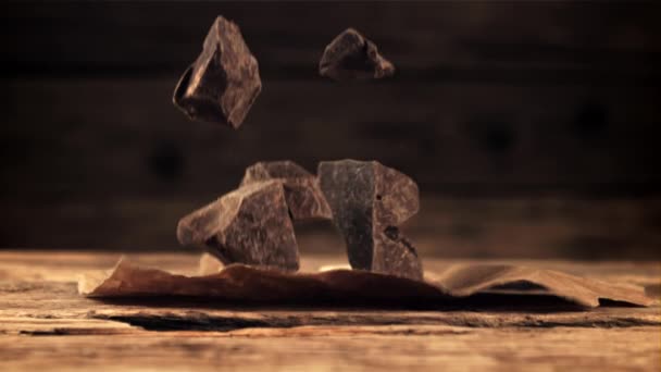 Super slow motion tombant morceaux de chocolat noir amer sur une table en bois. — Video