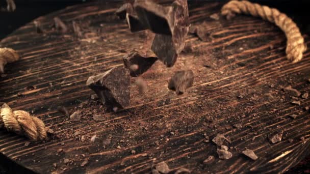Super slow motion vallende stukjes donkere, bittere chocolade op een houten plank. — Stockvideo