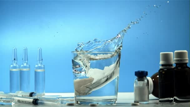 W szklance wody spada tabletka z rozpryskami. Nagrywane jest w zwolnionym tempie 1000 klatek na sekundę. — Wideo stockowe