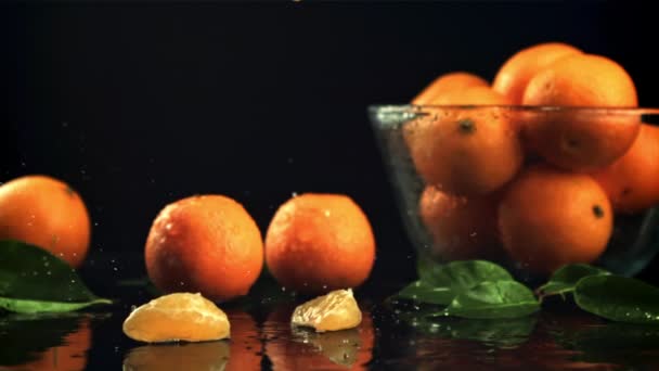 Кусочки спелых мандаринов падают на стол с брызгами воды. Замедленная съемка 1000 кадров в секунду. — стоковое видео