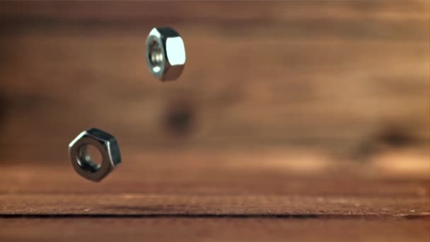 Des écrous métalliques tombent sur la table en bois. Filmé au ralenti 1000 images par seconde. — Video
