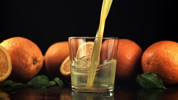Un chorro de jugo de naranja con salpicaduras vierte en el vaso. Filmado en cámara lenta 1000 fps. — Vídeo de stock