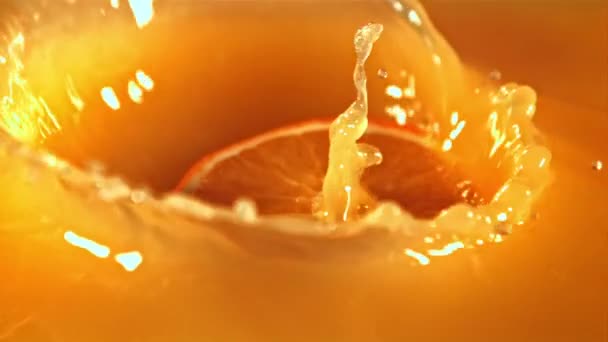 Un trozo de naranja fresca cae en el jugo de naranja con salpicaduras.Filmado en una cámara de alta velocidad a 1000 fps. — Vídeo de stock