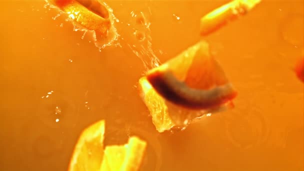 Stukken verse sinaasappel vallen in sinaasappelsap met spetters. Gefilmd op een hoge snelheidscamera met 1000 fps. — Stockvideo