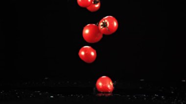Taze domatesler masaya su sıçratarak düşer. Siyah bir arka planda. Film yavaş çekimde 1000 fp..