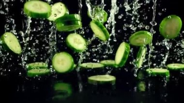 Taze salatalıklı su damlaları uçar ve düşer. Siyah bir arkaplanda. Ağır çekim 1000 fp..