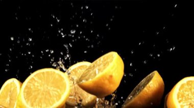 Sulu limon parçaları su damlatarak yukarı uçar ve aşağı düşer. Siyah bir arka planda. Film yavaş çekimde 1000 fp..