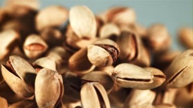 Bir şam fıstığı yığını yükselir ve düşer. Mavi arka planda. 1000 fps hızla yüksek hızlı bir kamerayla çekildi..