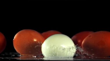 Yumurta su damlalarıyla masaya düşer. Siyah bir arka planda. 1000 fps hızla yüksek hızlı bir kamerayla çekildi..