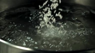 Çiğ pirinç kaynar suyun içine düşer. Makro arka plan. Film yavaş çekimde 1000 fp..