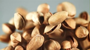 Bir şam fıstığı yığını yükselir ve düşer. Mavi arka planda. 1000 fps hızla yüksek hızlı bir kamerayla çekildi..