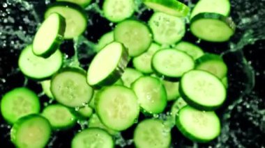 Taze salatalık parçaları ve su damlaları havada uçuşuyor ve dönüyor. Siyah bir arka planda. Üst Manzara. Film yavaş çekimde 1000 fp..