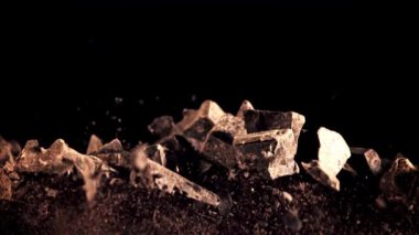 Bir yığın çikolata parçası yükselir ve düşer. Siyah bir arka planda. Film yavaş çekimde 1000 fp..