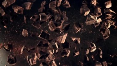 Çikolata parçaları havalanıyor ve uçuşta dönüyor. Üst Manzara. Karanlık bir arka plana karşı. Film yavaş çekimde 1000 fp..