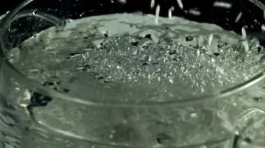 Çiğ pirinç kaynar suyun içine düşer. Makro arka plan. Film yavaş çekimde 1000 fp..