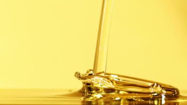 Bir jet zeytinyağı sıçrama ile düşer. Sarı arka planda. Film yavaş çekimde 1000 fp..