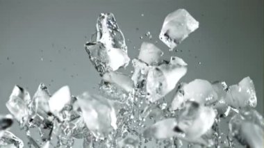 Su damlaları olan buz parçaları yükselir ve düşer. Gri bir arka planda. 1000 fps hızla yüksek hızlı bir kamerayla çekildi..