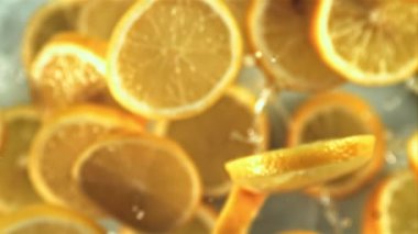 Bir damla suyla birlikte limon dilimleri uçuşta yavaşça döner. Beyaz bir arka planda. Üst Manzara. Film yavaş çekimde 1000 fp..
