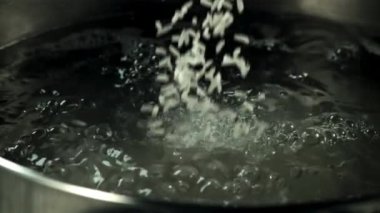 Çiğ pirinç kaynar suyun içine düşer. Makro arka plan. Film yavaş çekimde 1000 fp..
