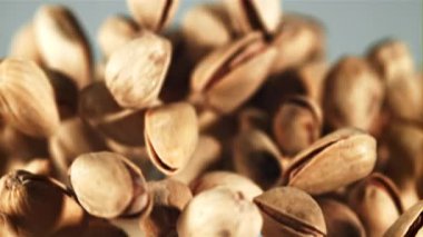 Bir şam fıstığı yığını yükselir ve düşer. Mavi arka planda. 1000 fps hızla yüksek hızlı bir kamerayla çekildi..