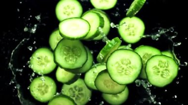 Taze salatalık parçaları bir damla suyla uçuyor. Siyah bir arkaplanda. 1000 fps hızla yüksek hızlı bir kamerayla çekilmiş..