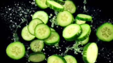 Taze salatalık parçaları ve su damlaları havada uçuşuyor ve dönüyor. Siyah bir arka planda. Üst Manzara. Film yavaş çekimde 1000 fp..