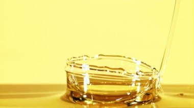 Bir jet zeytinyağı sıçrama ile düşer. Sarı arka planda. Film yavaş çekimde 1000 fp..