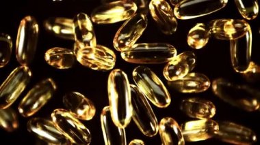 Omega 3 kapsülleri uçuşta döner. Siyah bir arka planda. Film yavaş çekimde 1000 fp..