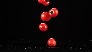 Taze domatesler masaya su sıçratarak düşer. Siyah bir arka planda. Film yavaş çekimde 1000 fp..