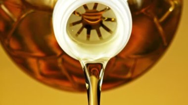 Zeytinyağı şişeden dökülür. Sarı arka planda. Film yavaş çekimde 1000 fp..