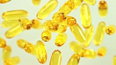 Omega 3 vitamin kapsülleri uçuşta yavaşça döner. Beyaz bir arka planda. Film yavaş çekimde 1000 fp..