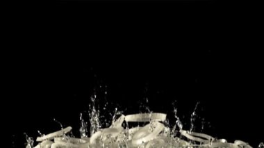 Dilimlenmiş soğan halkalarından oluşan bir yığın su damlaları yükselir ve aşağı düşer. Siyah bir arka planda. 1000 fps hızla yüksek hızlı bir kamerayla çekildi..