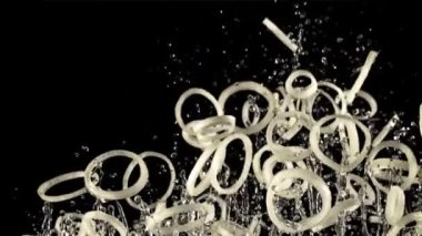 Soğan halkaları ve su damlaları havada uçuşuyor ve dönüyor. Siyah bir arka planda. Film yavaş çekimde 1000 fp..