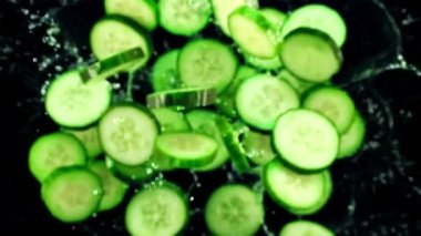 Taze salatalık parçaları ve su damlaları havada uçuşuyor ve dönüyor. Siyah bir arka planda. Üst Manzara. Film yavaş çekimde 1000 fp..