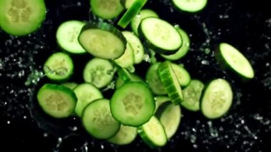 Taze salatalık parçaları ve su damlaları havada uçuşuyor ve dönüyor. Siyah bir arka planda. Üst Manzara. Film yavaş çekimde 1000 fp..