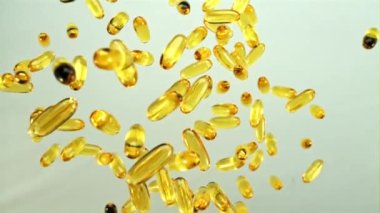 Omega 3 vitamin kapsülleri yukarı uçar ve döner. Gri bir arka planda. Üst Manzara. Film yavaş çekimde 1000 fp..