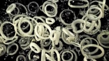 Soğan halkaları ve su damlaları yukarı uçar ve aşağı düşer. Üst Manzara. Siyah bir arka planda. Film yavaş çekimde 1000 fp..