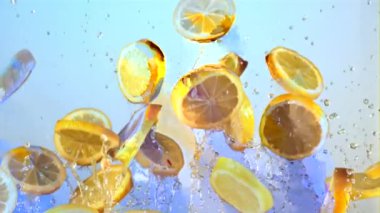İçinde su olan limon parçaları uçar ve düşer. Mavi arka planda. Film yavaş çekimde 1000 fp..