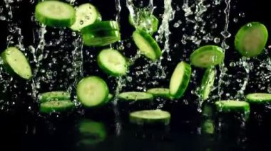 Taze salatalıklı su damlaları uçar ve düşer. Siyah bir arkaplanda. Ağır çekim 1000 fp..