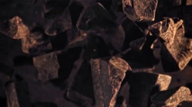 Çikolata parçaları havalanıyor ve uçuşta dönüyor. Üst Manzara. Karanlık bir arka plana karşı. Film yavaş çekimde 1000 fp..