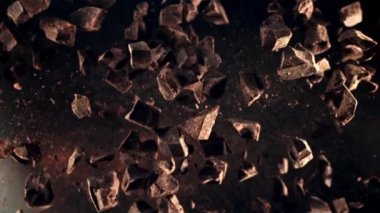 Çikolata parçaları havalanıyor ve uçuşta dönüyor. Üst Manzara. Karanlık bir arka plana karşı. Film yavaş çekimde 1000 fp..