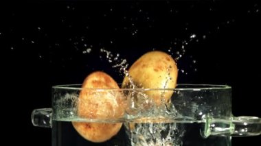 Patatesler su dolu bir kaba dökülür. Siyah bir arka planda. Film, yavaş çekim 1000 fp. Yüksek kaliteli FullHD görüntüler