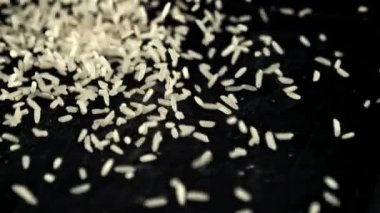 Pişmemiş bir pirinç yığını masaya düşer. Siyah bir arka planda. Film yavaş çekimde 1000 fp..