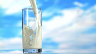 Süt bir girdapta bardağa dökülür. Mavi bir arkaplanda. Ağır çekim 1000 fp..