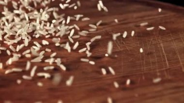 Pişmemiş pirinç masaya saçılmış ve döndürülmüş. Tahta bir arka planda. 1000 fp 'lik yüksek hızlı bir kamerayla çekildi..