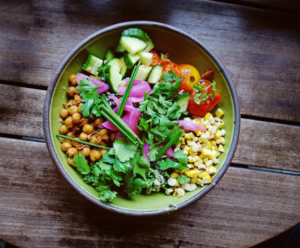 Healthy grain bowl topped with chickpeas, tomatoes, corn, cilantro, onions and cucumbers
